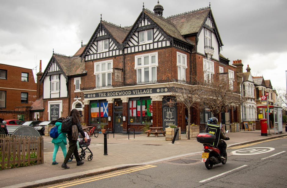 A large, historic red brick building with ornate architectural details, including a central arched window with decorative tracery and smaller towers with pointed rooftops on either side, situated at t